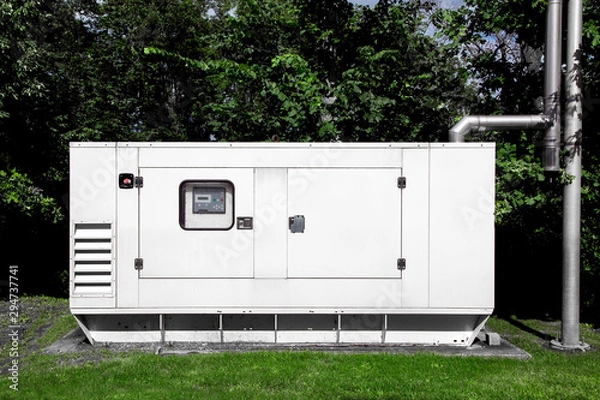 Obraz backup diesel electric power emergency generator mounted on a green lawn with green trees and a separate exhaust pipe for environmental safety.