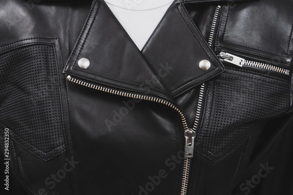 Fototapeta Black leather jacket with perforated elements. Metal zippers, clasps and buttons. Classic clothes for biker. Detailed closeup view. White t-shirt.