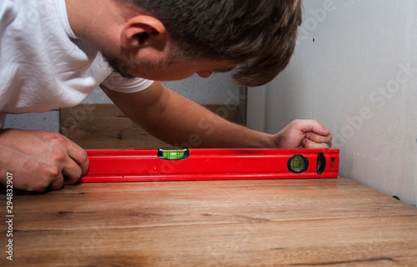 Fototapeta young guy in a white T-shirt makes repairs in the bathroom using modern tools for gluing tiles. The concept of home work, repair and construction
