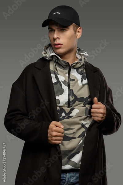 Fototapeta Medium close-up shot of a short-haired European man dressed in a dazzle hooded top, a black jacket and a black baseball cap with an embroidered black lettering "New York".