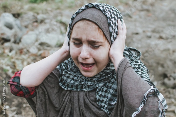 Obraz a refugee child in the war, a Muslim girl with a dirty face on the ruins, the concept of peace and war, the child is crying and waiting for help.