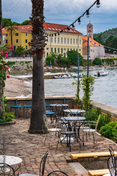 Fototapeta An empty beach bar terrace after rain with a view of the port with sailing boats and the old town, picturesque scene, Vis island, Croatia, Europe. Summer travel