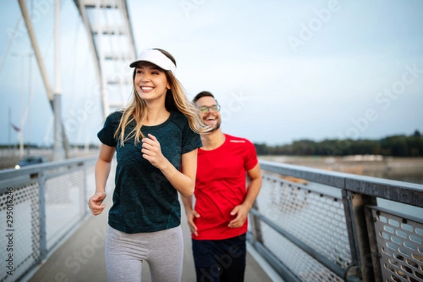 Fototapeta Early morning workout. Happy couple running across the bridge