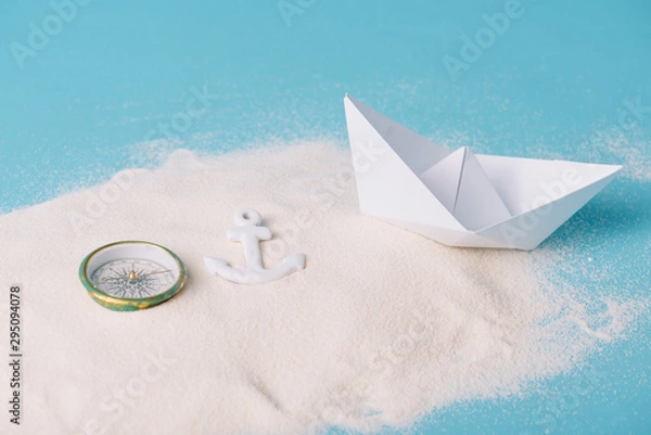 Fototapeta sand with paper boat, compass and anchor on blue background