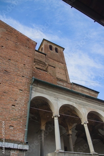 Fototapeta Part of an old building, thin columns of the church and a tower made of small bricks, an Italian building, bottom view. A bright sunny day, no people.