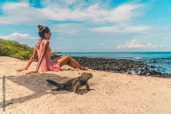 Fototapeta Galapagos beach iguana and woman tourist on beach. Natural wildlife shot in San Cristobal, Galapagos. Beautiful beach with ocean sea background. Wild animal in nature.