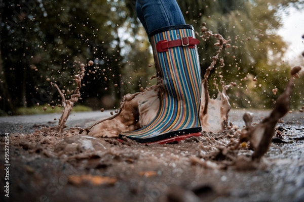 Obraz A woman wearing rubber boots jumps into a puddle on a cold autumn day.