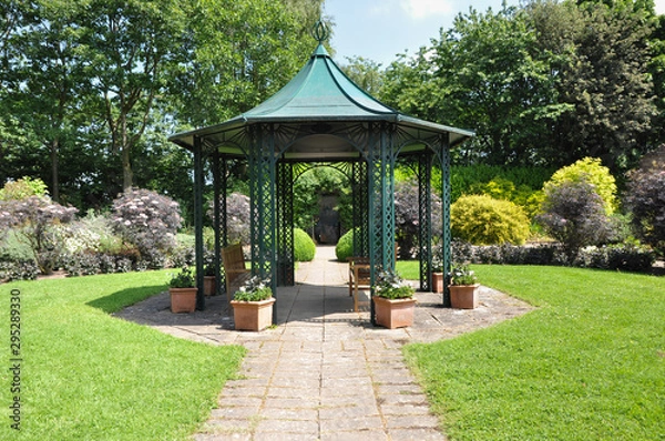 Obraz Large  hexagonal gazebo provides shade for seating inEnglish formal garden 