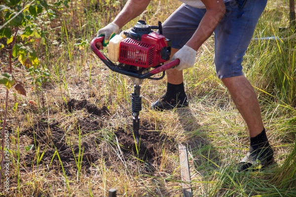 Obraz Worker drills the ground for the fence