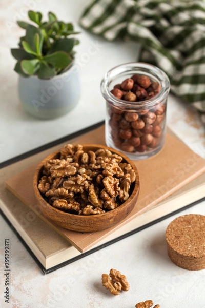 Fototapeta a handful of walnuts in a wooden plate, a handful of hazelnuts in a quilted jar on a light background with a green plant in the background