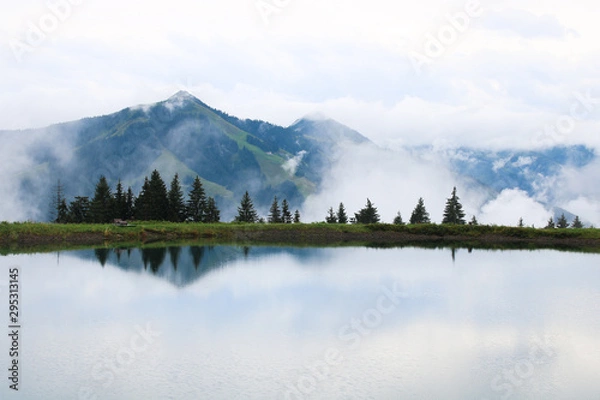 Fototapeta Hike to a mountain lake in the Alps in Austria, surrounded by white clouds, and a beautiful view of the reflection in the water