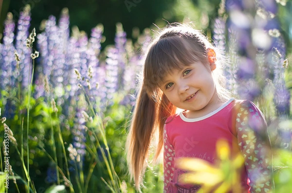 Fototapeta Portrait of little girl in flowers. Cute smiling kid in Blooming Lupine flowers field. Lupinus polyphyllus field