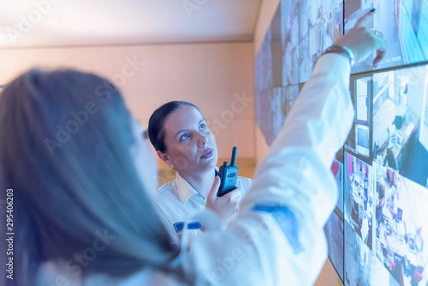 Fototapeta Security guard monitoring modern CCTV cameras in surveillance room. Female security guard in surveillance room. Female security guard holding portable radio in hand at workplace.