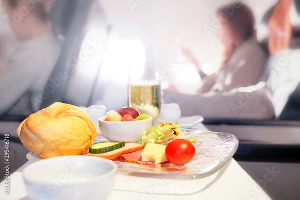 Fototapeta Airplane breakfast food in business class against passenger cabin interior blurred background. Side closeup view of aircraft meal starters on tray table. Luxury jet plane air travel service concept