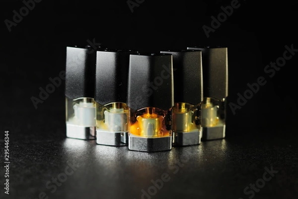 Fototapeta e-juice vape refill pods with liquids of different shades of orange yellow, black background isolated close up
