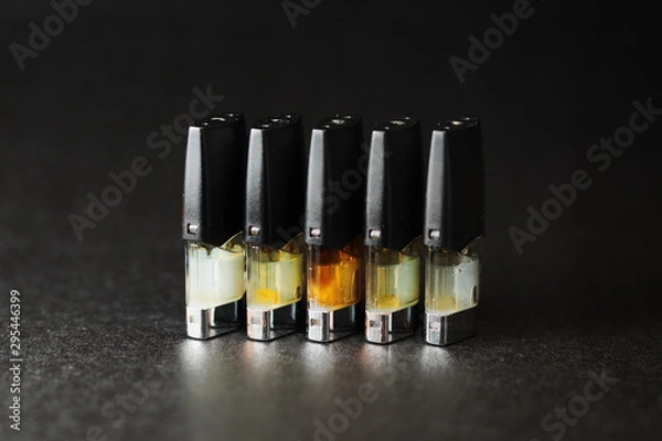 Fototapeta e-juice vape refill pods with liquids of different shades of orange yellow, black background isolated close up