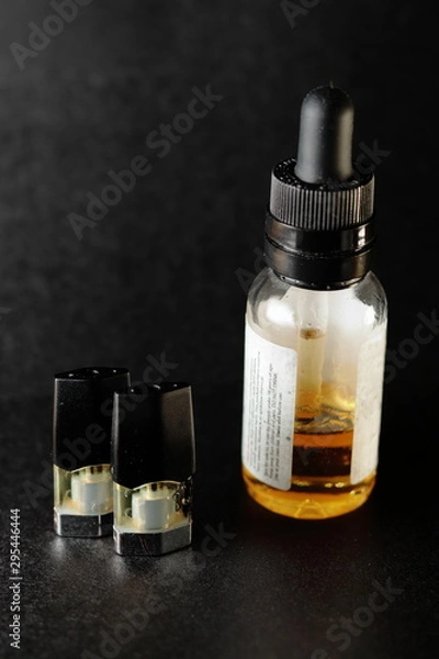 Fototapeta e-juice vape refill pods with with a bottle of orange e-liquid, isolated close up black background