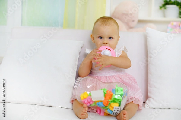 Fototapeta  Sweet baby girl playing with toys on sofa, looking at camera             
