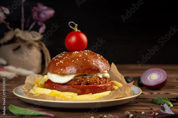 Fototapeta cheeseburger decorated with cherry tomato on a plate on a wooden table
