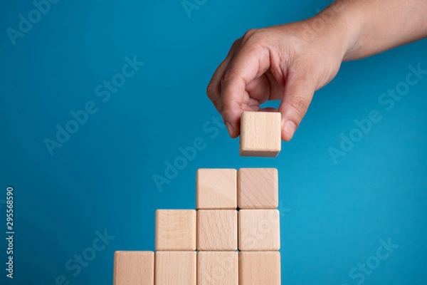 Fototapeta Hand arranging block on blue background. Business concept on progress or building something.