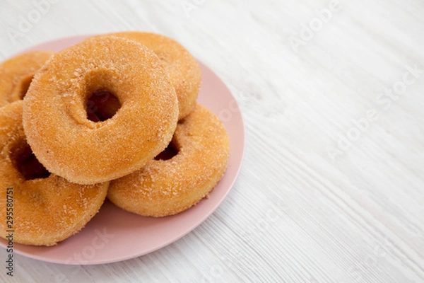 Fototapeta Homemade autumn apple donuts on a pink plate on a white wooden surface, low angle view. Copy space.