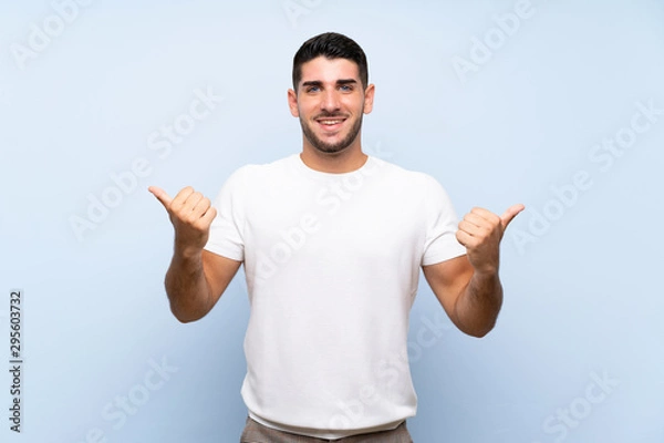 Fototapeta Caucasian handsome man over isolated blue background with thumbs up gesture and smiling