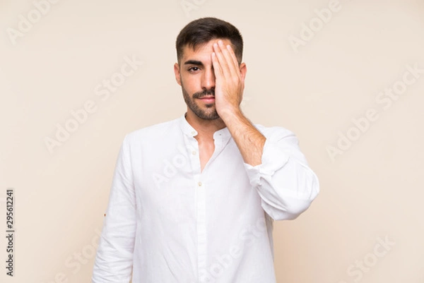 Fototapeta Handsome man with beard over isolated background covering a eye by hand