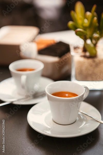 Fototapeta Close up. The small white ceramic mug (cup) with Italian espresso (coffee) on a table with a saucer and a metal spoon in a local Italian bar (coffee shop) in Milan, Lombardy, Italy. Beverage.