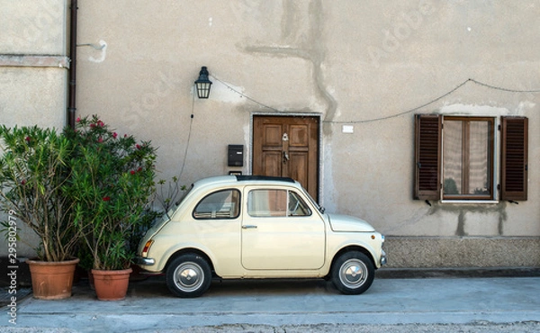 Obraz Small vintage italian car. Beige color old car in front of old house facade and flowers..