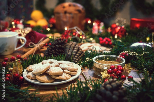 Obraz Stół świątecznych składników z ciasteczkami pośrodku na drewnianej desce, w towarzystwie pomarańczy, panettone, cynamonu, sosny. Świąteczna dekoracja sosnowa na czerwonym tle rustykalnym