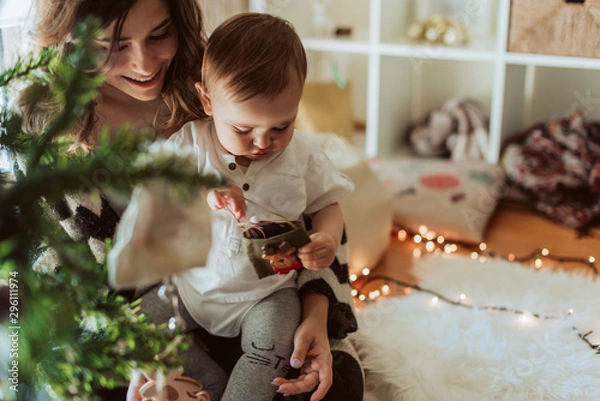 Obraz Mother and baby playing around the Christmas Tree