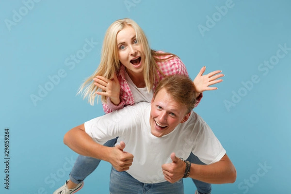 Fototapeta Young fun couple two friends guy girl in white pink empty blank design t-shirts posing isolated on pastel blue background studio portrait. People lifestyle concept. Mock up copy space. sitting on back