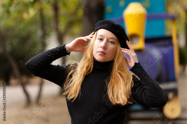 Obraz Blondy girl in black sweater and beret stands in the autumn in the park