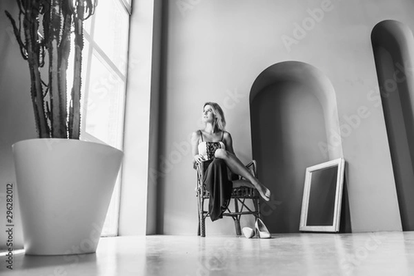 Fototapeta young pretty and seductive girl is in a big spacious room with big windows and sitting on a chair