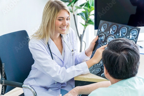 Obraz Caucasian female doctor showing Asian patient the film of MRI tomography scan of the brain.