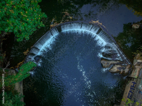 Fototapeta Aerial, Top-Down View of a Man-Made Waterfall on a River - in a Secluded Spot in the City, Surrounded by Lush Green Trees