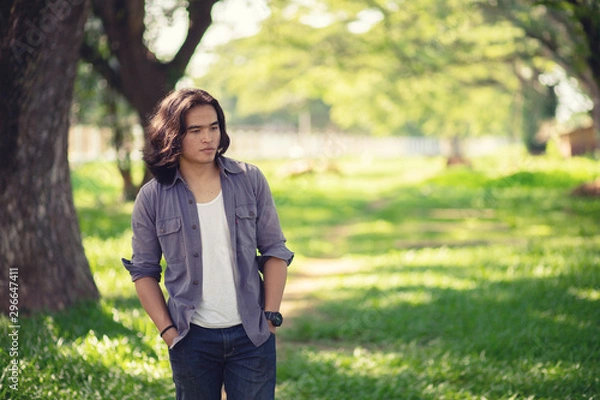 Fototapeta Asian long hair man Walking in the garden The background is a tree and the sunlight in autumn.
