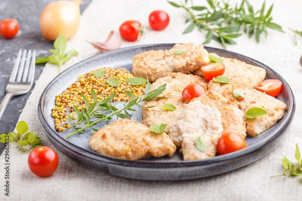 Fototapeta Fried pork chops with tomatoes and herbs on a gray ceramic plate on a black concrete background. side view, selective focus.