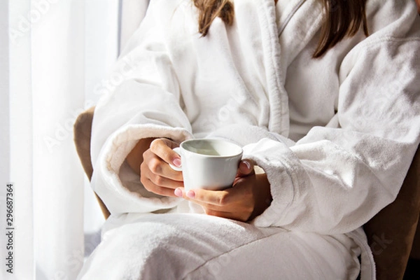 Obraz A girl in a white coat is drinking morning coffee.