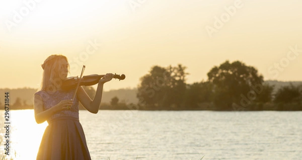 Fototapeta romantic silhouette of young woman with a violin at dawn on river bank, elegant girl playing a musical instrument on nature, concept music and inspiration