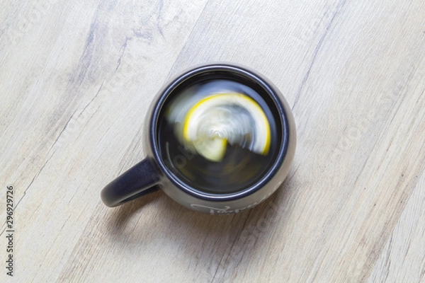 Fototapeta Green tea with lemon twisted in a black cup on a wooden parquet