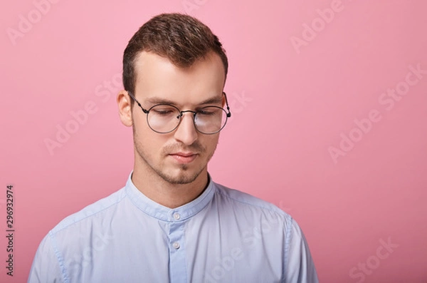 Fototapeta A decent young man in a sky blue shirt and computer glasses stands on a pink background. Student, businessman, employee of the year. Happy. look