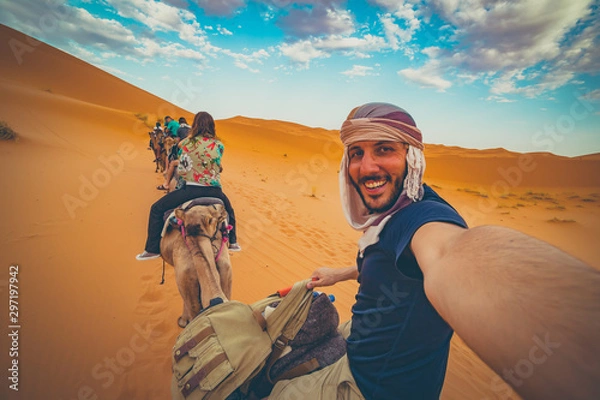 Fototapeta happy nomad man taking crazy selfie during camel riding in Sahara Desert, Merzouga, Morocco