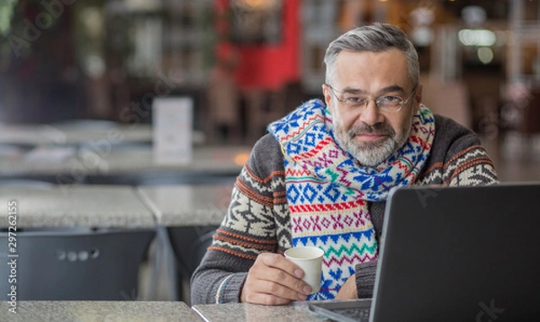 Obraz  Man wearing autumn or winter clothes, scarf sitting in a cafe working  using laptop