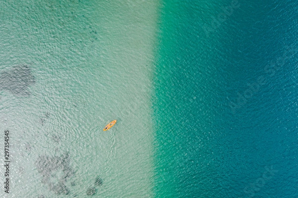 Fototapeta Top down aerial view of orange kayak with two woman on turquoise water at shallow sea shore. Kayaking during summer vacation. High angle background with copy space. Primorsky Krai, Far East, Russia