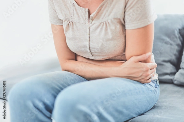 Fototapeta Woman with  stomach issues / problems while lying on the couch.