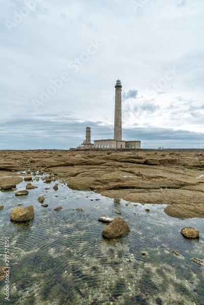Obraz tall stone lighthouse with rocky shore tidal pools in foreground under a stormy sky