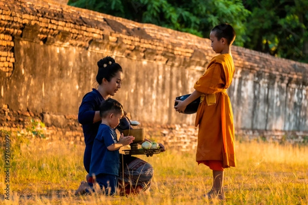 Fototapeta Monk Buddhist elder Novice. The family Children woman putting food offerings in a monk's alms bowl and a woman prostrating oneself to respect worship monks, monks walking routine every morning.
