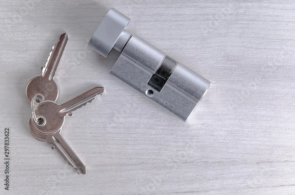 Fototapeta Lock core and door keys on a light background. Repair in the house. Installing a new lock on the door. Spare parts for the door on a gray wooden table.