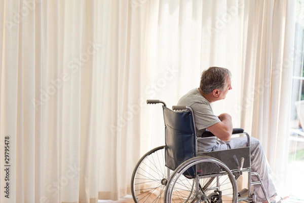 Fototapeta Man in his wheelchair looking out the window